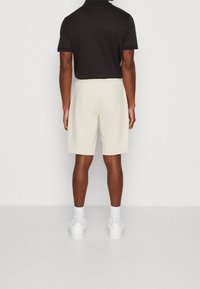 Helle beigefarbene Shorts mit elastischem Bund, kombiniert mit einem schwarzen Polohemd. Weiße Socken und Schuhe vervollständigen das Outfit.