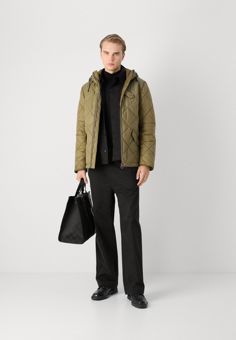 Giacca imbottita verde oliva con cappuccio, camicia nera, pantaloni neri e borsa nera texture. Le scarpe sono formali nere. Sfondo bianco semplice.