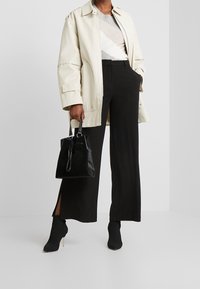 Giacca oversize color crema chiaro, top grigio a fantasia, pantaloni neri a gamba larga con fessure laterali e borsa nera. Stivali neri chunky alla caviglia con tacco.