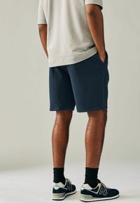 Pantalones cortos azul marino oscuro con bolsillos laterales, confeccionados en una tela suave. Combinados con calcetines negros y zapatillas New Balance con toques en crema.