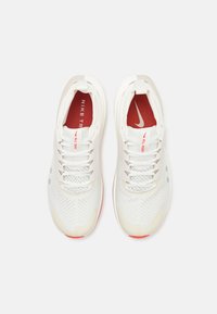 Weiße Sportschuhe mit einem Obermaterial aus Mesh, rotem Innenfutter und einfarbigen Schnürsenkeln. Mit Nike-Branding und einer strukturierten Sohle für guten Halt.