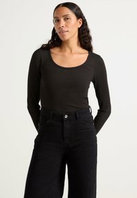 Maglietta nera a maniche lunghe con scollatura ampia a barca, abbinata a jeans neri a vita alta. Texture sottile e design aderente.