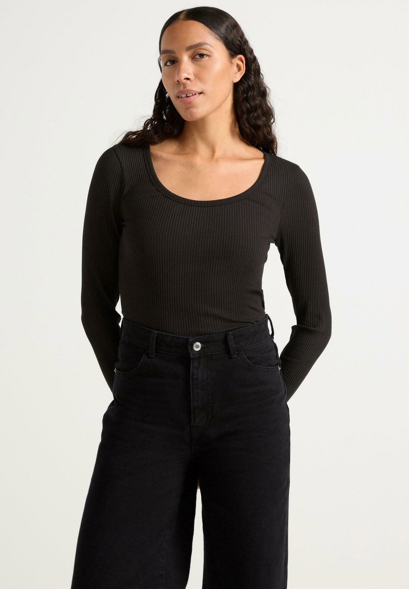 Maglietta nera a maniche lunghe con scollatura ampia a barca, abbinata a jeans neri a vita alta. Texture sottile e design aderente.