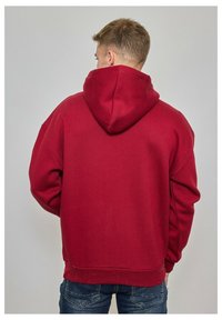 Sweat-shirt à capuche bordeaux avec une coupe décontractée, des poignets et un ourlet côtelés. Texture douce, poche kangourou non visible de l'arrière.