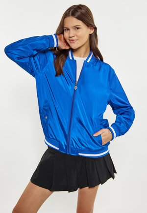 Giacca bomber blu in materiale lucido con polsini e orlo a strisce bianche, dotata di chiusura con zip e tasche laterali.