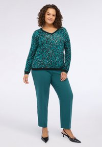 Pulover teal cu un model, cu decolteu în V și mâneci lungi, asortat cu pantaloni verzi cu croială dreaptă. Pantofii cu toc negri completează ținuta.