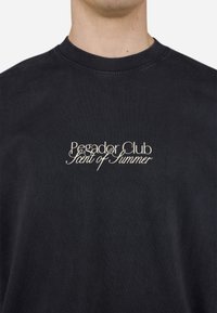 Tricou din bumbac negru cu guler rotund. Textul alb centrat spune "Pegador Club Aromă de Vară" într-un font cursiv.