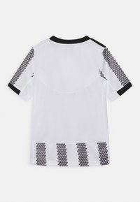 T-shirt de sport blanc à manches courtes, avec des accents noirs au col et aux manches, et un motif géométrique noir le long des côtés et de l'ourlet.