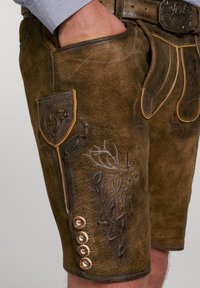 Bruna lädershorts med prägling av en hjortdesign, sidofickor och dekorativa knappar längs fållen. Texturerad yta med accentuerande sömmar.