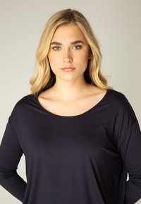Navy-blaues Langarmoberteil mit weitem Halsausschnitt und lässiger Passform, aus glattem, leichtem Stoff gefertigt. Minimalistisches Design ohne Muster.