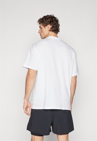 White cotton t-shirt with short sleeves, crew neck, and a relaxed fit. Paired with black athletic shorts. Simple design, no patterns or logos.