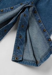 Denim-kangas eri sinisävyissä sisältää pronssinvärisiä nappeja reunojen varrella. Kangas on pehmeä ja siinä on näkyviä ompelusaumoja.