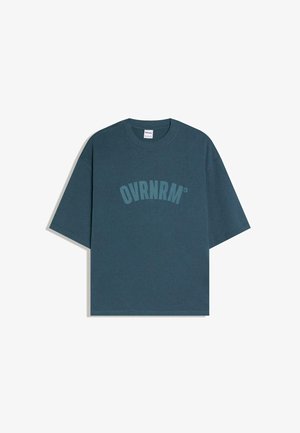 Ciemnoturkusowy, luźny T-shirt z krótkim rękawem i okrągłym dekoltem, z nadrukiem "OVRNRM" w pasującym kolorze na wysokości klatki piersiowej.