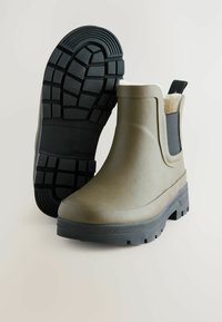 Olijfgroene waterdichte enkellaarsjes van rubber met een zwarte rubberen zool, voorzien van elastische zijkanten en een gestructureerd grippatroon.