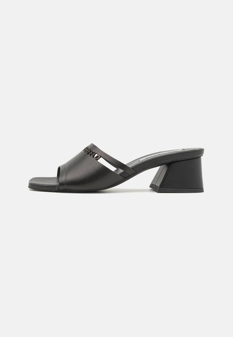Mules noires à talons avec une finition lisse et mate, bout ouvert, et des accents de découpes décoratives sur le dessus. Talon bloc de forme géométrique.