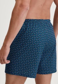 Costumi da bagno da uomo in tessuto blu scuro con un motivo circolare in blu chiaro e grigio. Presentano una vita elasticizzata e una vestibilità comoda.