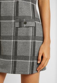 Grijze geruite jurk met een gestructureerde stof, zwart-witte strepen, een knoopzak en een getailleerde pasvorm.