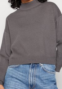 Un pull en maille grise avec un col montant, des épaules tombantes et un ourlet côtel�é, assorti à un jean en denim bleu taille haute.