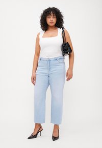 Light blue high-waisted jeans with a straight-leg fit, frayed hem, paired with a white square-neck sleeveless top and a black mini handbag.