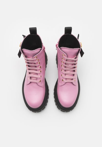 Botas de tobillo de cuero rosa con ojales dorados, cordones planos y una suela de goma negra gruesa. Presentan una cremallera lateral y una cinta para facilitar el calzado.