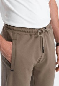 Taupe joggingbroek met een gestructureerde stof, voorzien van een trekkoord in de taille, zijzakken en contrasterende zwarte accenten.