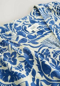 Gros plan du col d'une chemise en lin à motif floral bleu et blanc avec une étiquette de marque "next" cousue à l'intérieur.