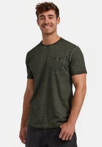 Dunkelgrünes T-Shirt mit kurzarm und Rundhalsausschnitt, ausgestattet mit einer Brusttasche und subtiler Textur. Hergestellt aus weichem, atmungsaktivem Material.