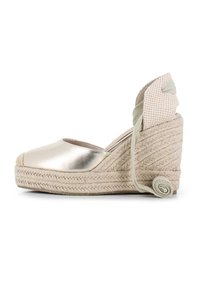 Espadrille de cuña metálica dorada con suela de yute trenzado, que presenta una parte trasera de lona y un detalle de lazada con un acento de cinta enrollada.