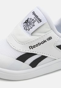 Bijela tenisica od mrežastog i sintetičkog materijala, s crnim prugama, Reebok logotipom i oznakom ukrašenom geometrijskim dizajnom.