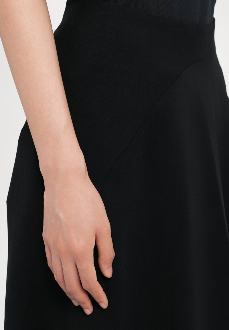 Black fabric skirt with a smooth texture, featuring a curved design seam. A hand rests gently on the skirt, showcasing its draping quality.