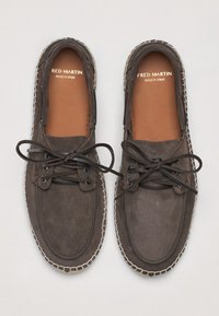 Zapatos de ante marrón con un diseño plano, punta redonda, cordones en la parte delantera y costuras en contraste a lo largo de la suela. Hechos en España.