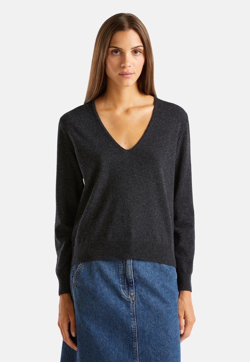 Ciemnoszary sweter w serek wykonany z miękkiego materiału, z długimi rękawami i lekko zwężającym się dołem, zestawiony z dżinsową spódnicą.