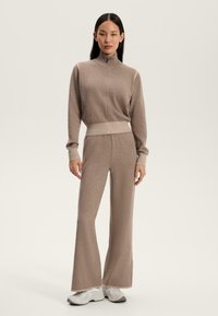 Completo a maglia marrone composto da un pullover con zip e polsini a coste abbinato a pantaloni a campana a vita alta. Il materiale è morbido con una consistenza liscia.