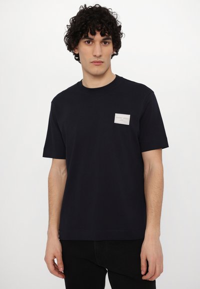 Tricou scurt cu manecă, de culoare albastru marin, fabricat din bumbac, având o eticheta mică gri pe piept, guler rotund și o croială lejeră.