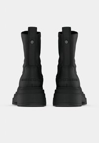 Mustad nilkkasaapad tekstuurse viimistlusega, millel on kõrge tald, vertikaalsed tõmblukud ja ümmargused riistvaradetailid.