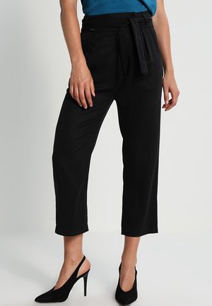 Black tailored trousers with a tied waistband, cropped length, and smooth texture. Paired with black high-heeled shoes.