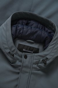 Siva jakna z gladkim zunanjim materialom in mornarsko modro prešito notranjostjo. Ima visok ovratnik, gumbne zaponke in nastavljiv vrvico.