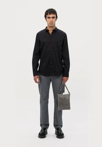 Zwarte button-up shirt, donkergrijze jeans, zwarte schoenen en een grijze geweven handtas. De outfit heeft een strakke design en een getailleerde pasvorm.