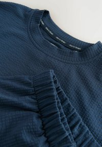 Mörkblå texturerad sweatshirt med rundad halsringning och ribbad krage. Har en samlad detalj på ärmen och ett subtilt randigt mönster.