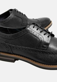 Černé kožené boty s texturovaným povrchem, detaily v brogue stylu, šněrovací design a kontrastní hnědá podrážka. Obsahují perforované akcenty.