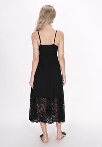 Rochie neagră cu bretele subțiri, corset ajustat și margine fluidă din dantelă. Dantela are modele florale complicate.