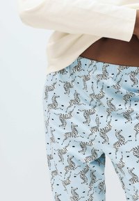 Lyseblå pyjamasbukser med sort-hvidt zebra mønster, med elastik i taljen og en blød, glat tekstur.