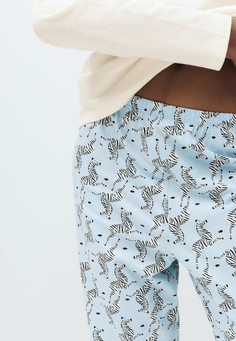Lyseblå pyjamasbukser med sort-hvidt zebra mønster, med elastik i taljen og en blød, glat tekstur.