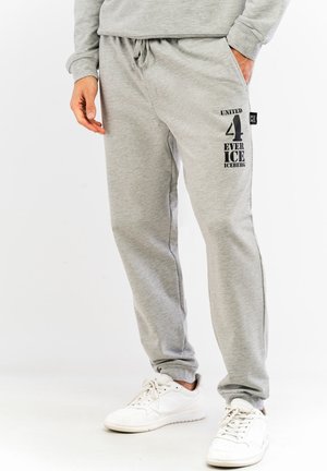 Graue Sweatpants aus weichem Material, mit Seitentaschen, einem Kordelzug-Bund und schwarzem Textgrafik auf dem linken Bein.