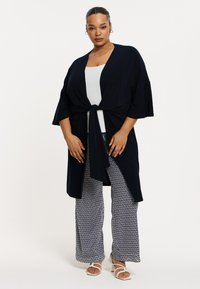 Kimono léger bleu marine avec un front noué, associé à un pantalon large à motifs présentant un design de lignes ondulées en bleu marine et blanc.