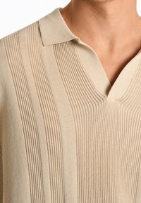 Beige stickad polo t-shirt med V-hals, prydd med vertikala ribbade ränder, strukturerat tyg och en mjuk krage.