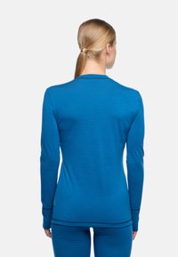 Blaue Langarmbluse aus glattem Stoff, mit Rundhalsausschnitt und kontrastierenden Nähten entlang der Ärmel und dem Saum.