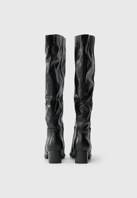 Botine negre până la genunchi, fabricate din piele netedă, cu un design lejer, tocuri pătrate și o textură moale. Stil minimalist, fără elemente de feronerie vizibile.