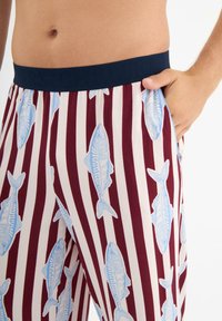 Katoenen loungebroek met een marineblauwe elastische tailleband, voorzien van blauwe vissenpatronen op crèmekleurige strepen, met een soepel en zacht textuur.