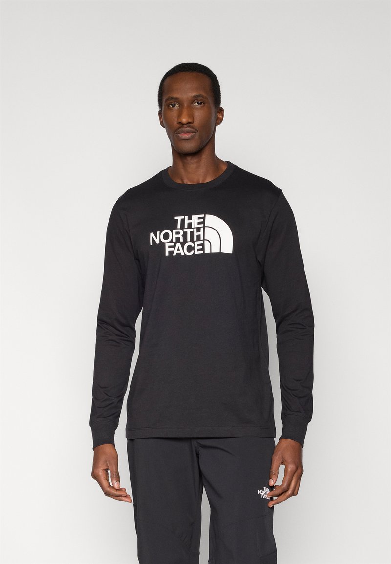 Μαύρο μακρυμάνικο μπλουζάκι με λευκό λογότυπο στο στήθος, στρογγυλή λαιμόκοψη και λεία υφή υφάσματος. Φορεμένο με παντελόνι που ταιριάζει.